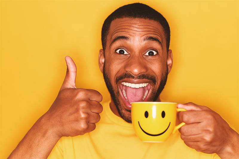 Happy guy giving a thumbs up, hold a smiley face cup will boost your mood.