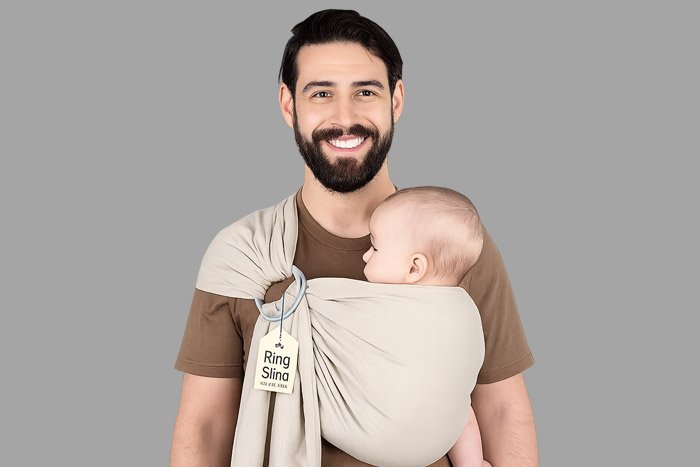 Smiling bearded father carrying baby in over the shoulder sling wrap.